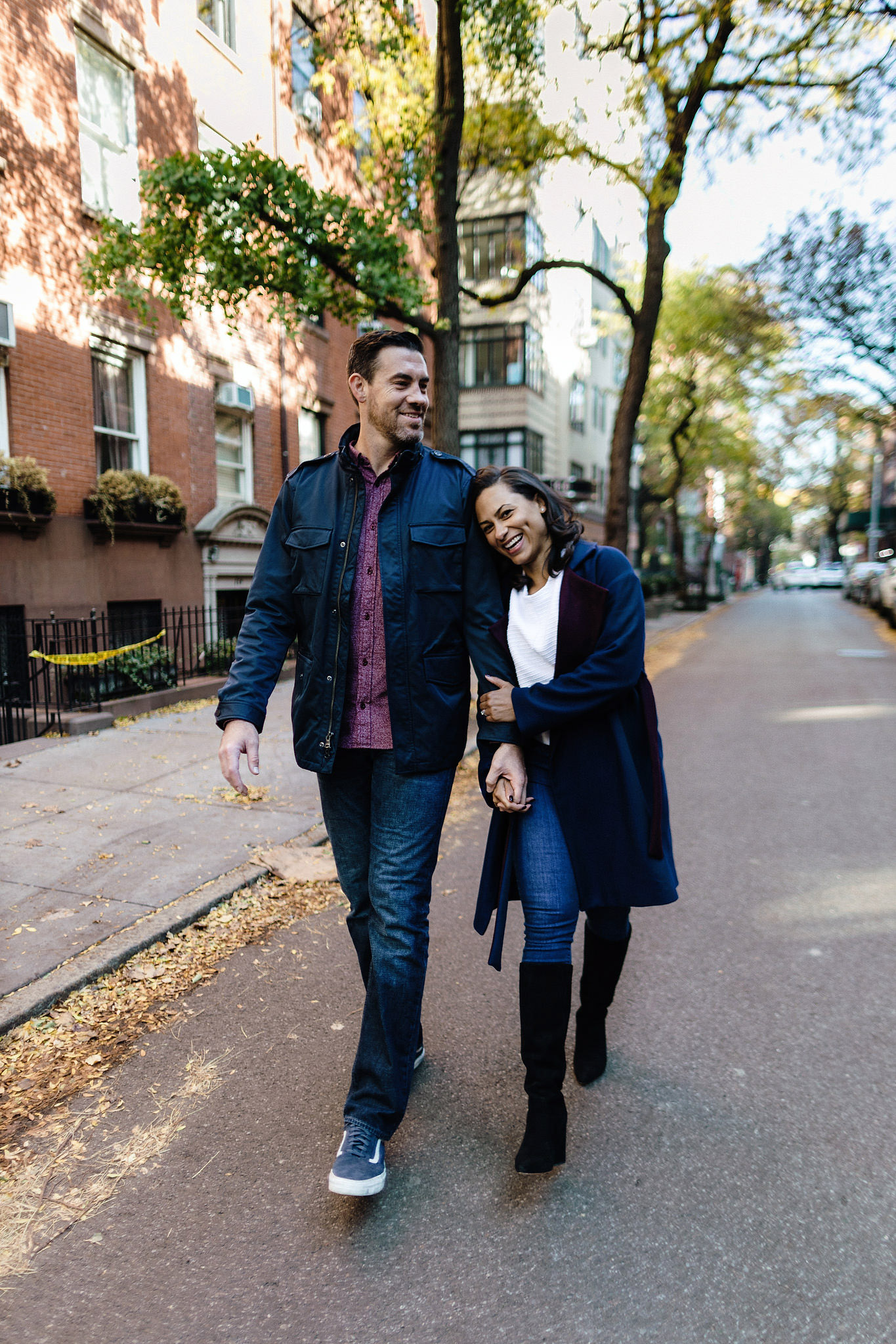 Man and woman in love stroll the streets in Brooklyn heights, laughing with each other while she holds onto his arm
