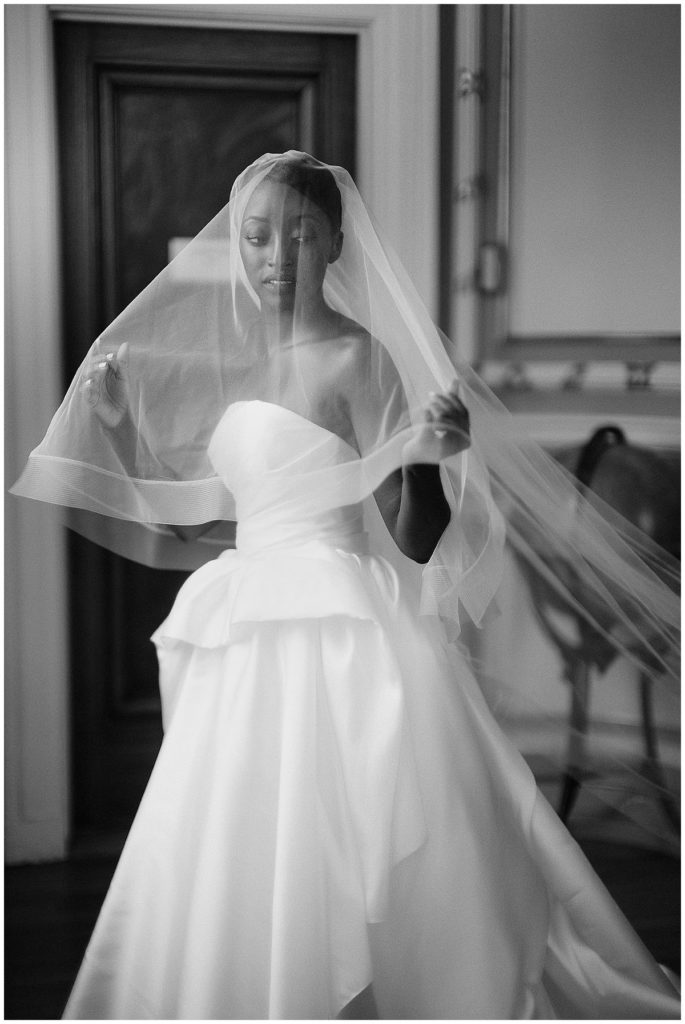 Stunning bride stands beneath her cathedral veil and looks off the side as the veil trails behind her.