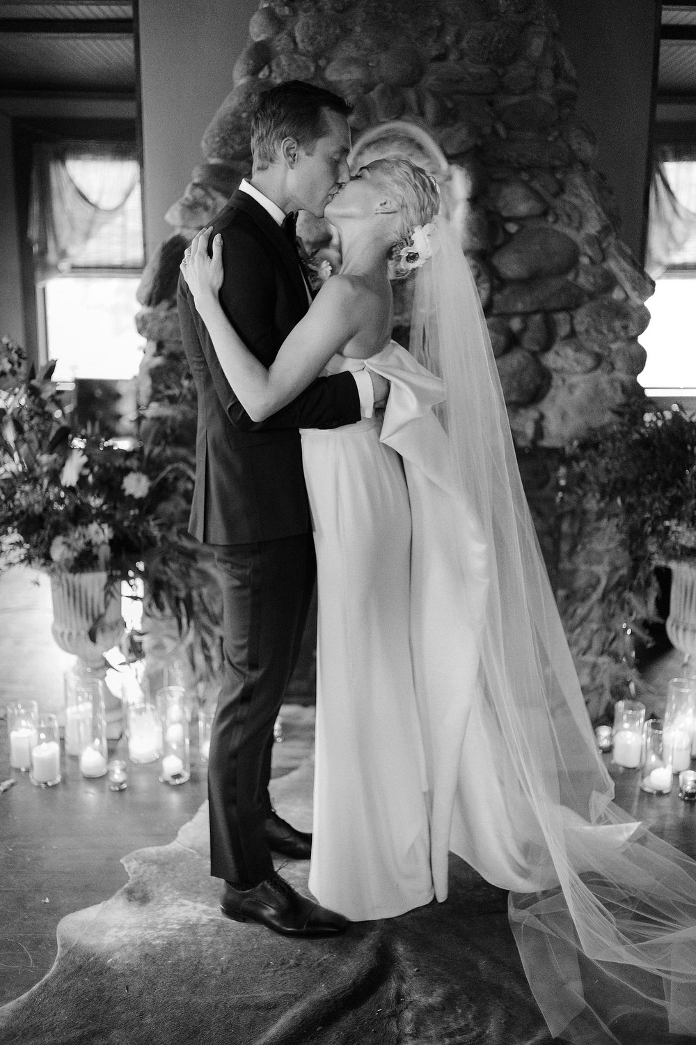 A happy husband and wife share their first kiss in front of the giant stone fireplace at Firefox Mountain House in New York.