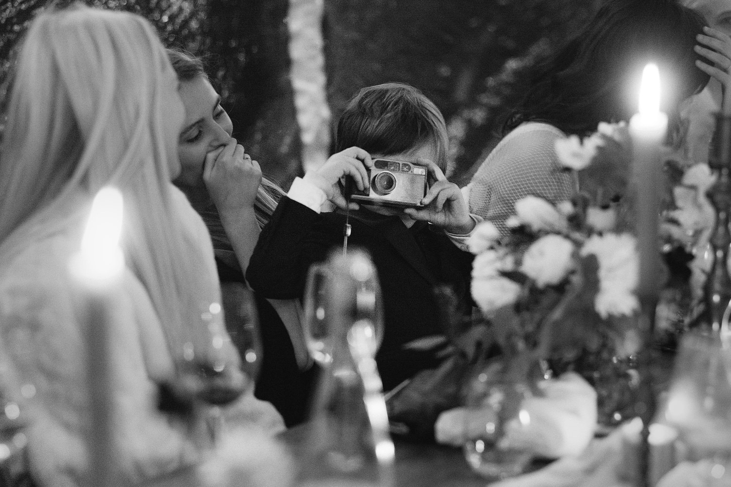 Little ring bearer takes a photo of the photographer with an old-fashioned point and shoot camera. Editorial Wedding at Firefox Mountain House in Upstate New York.