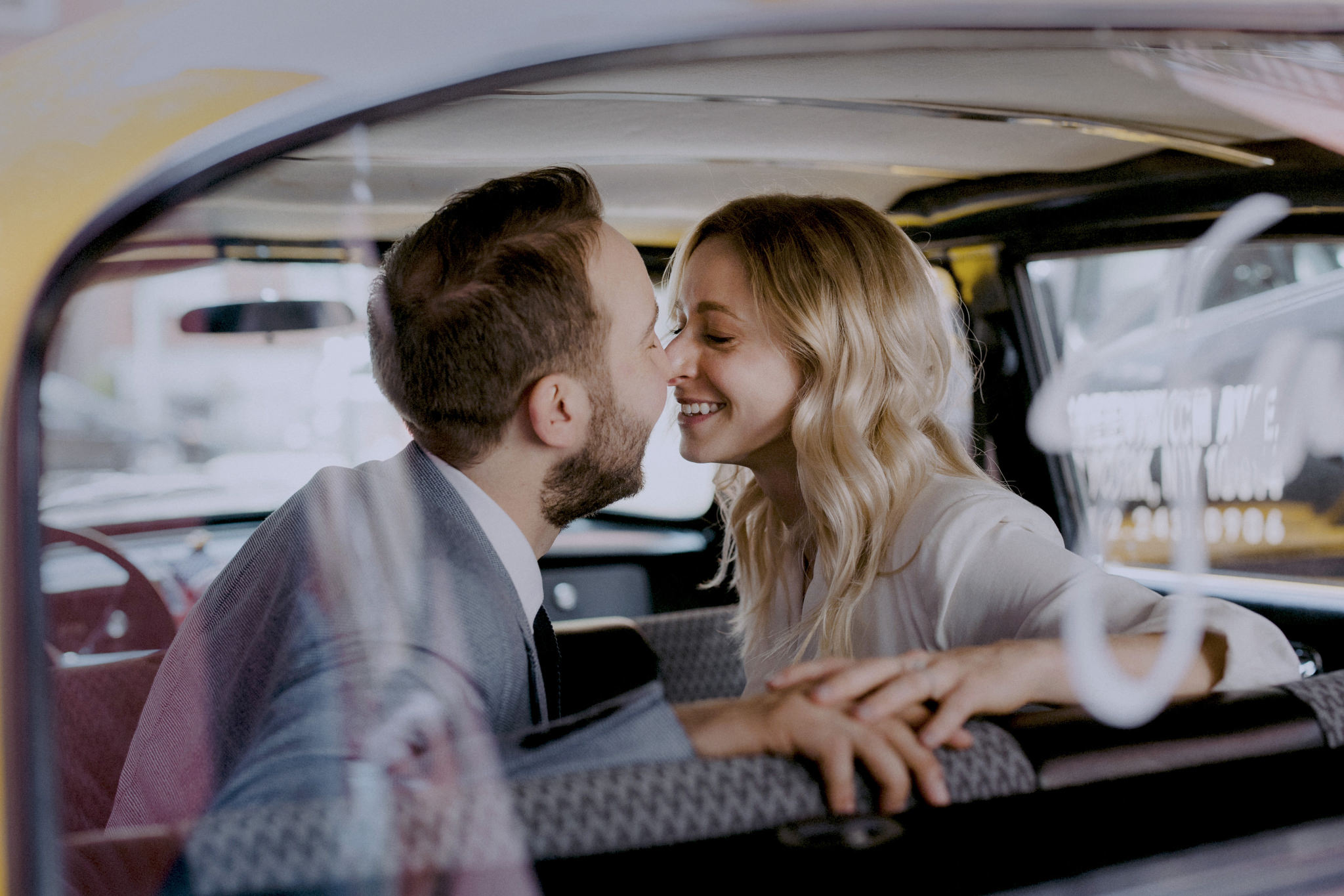 Married couple smiling at each other in the back of a vintage taxi on their wedding day.