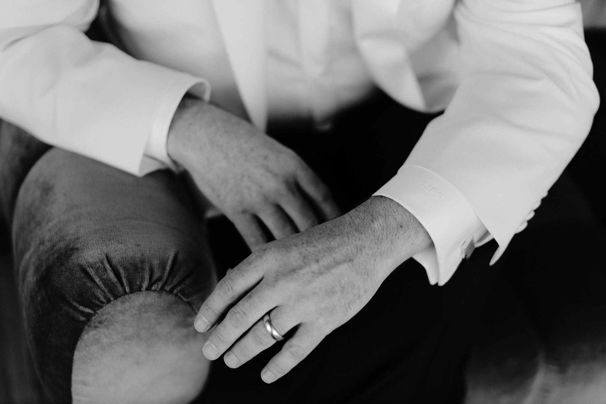 Close up view of mans hands with white suit jacket sleeves and wedding band