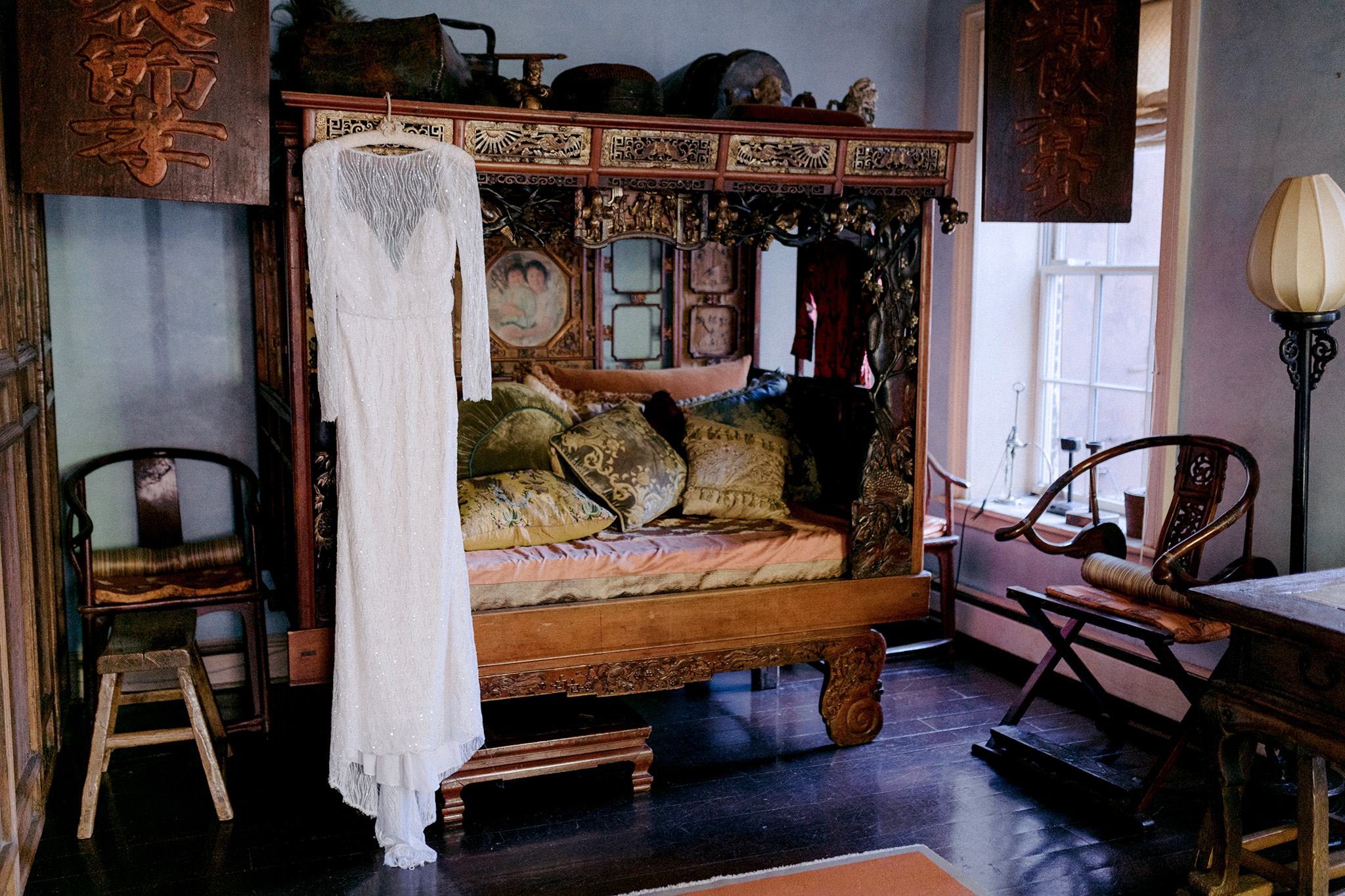 Long sleeve lace wedding dress hanging on antique canopy bench