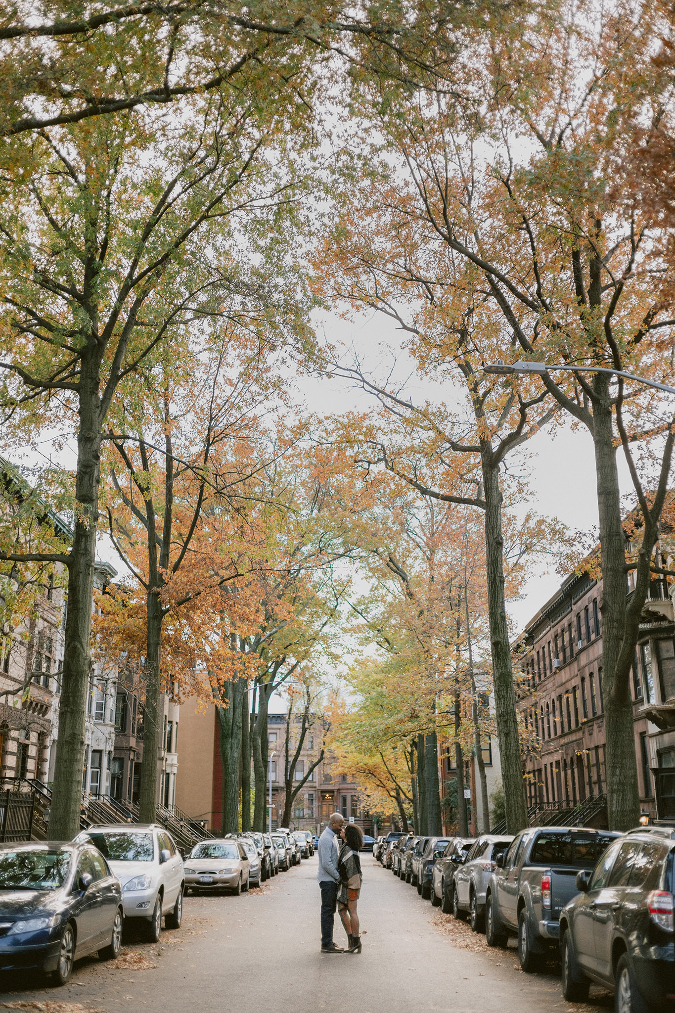 Engaged couple kissing in middle of tree lined New York City street