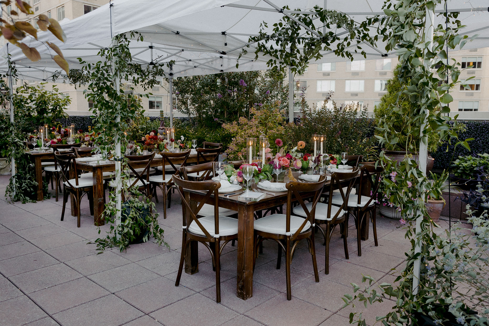 A rooftop patio with wooden tables and chairs surrounded by vines and pink flowers