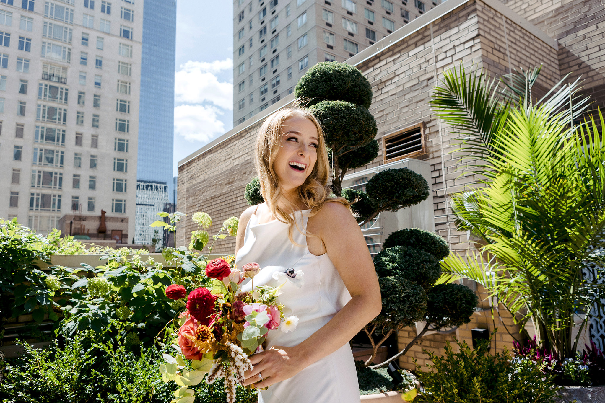 A bride holding her bouquet, laughing on a rooftop in Manhattan