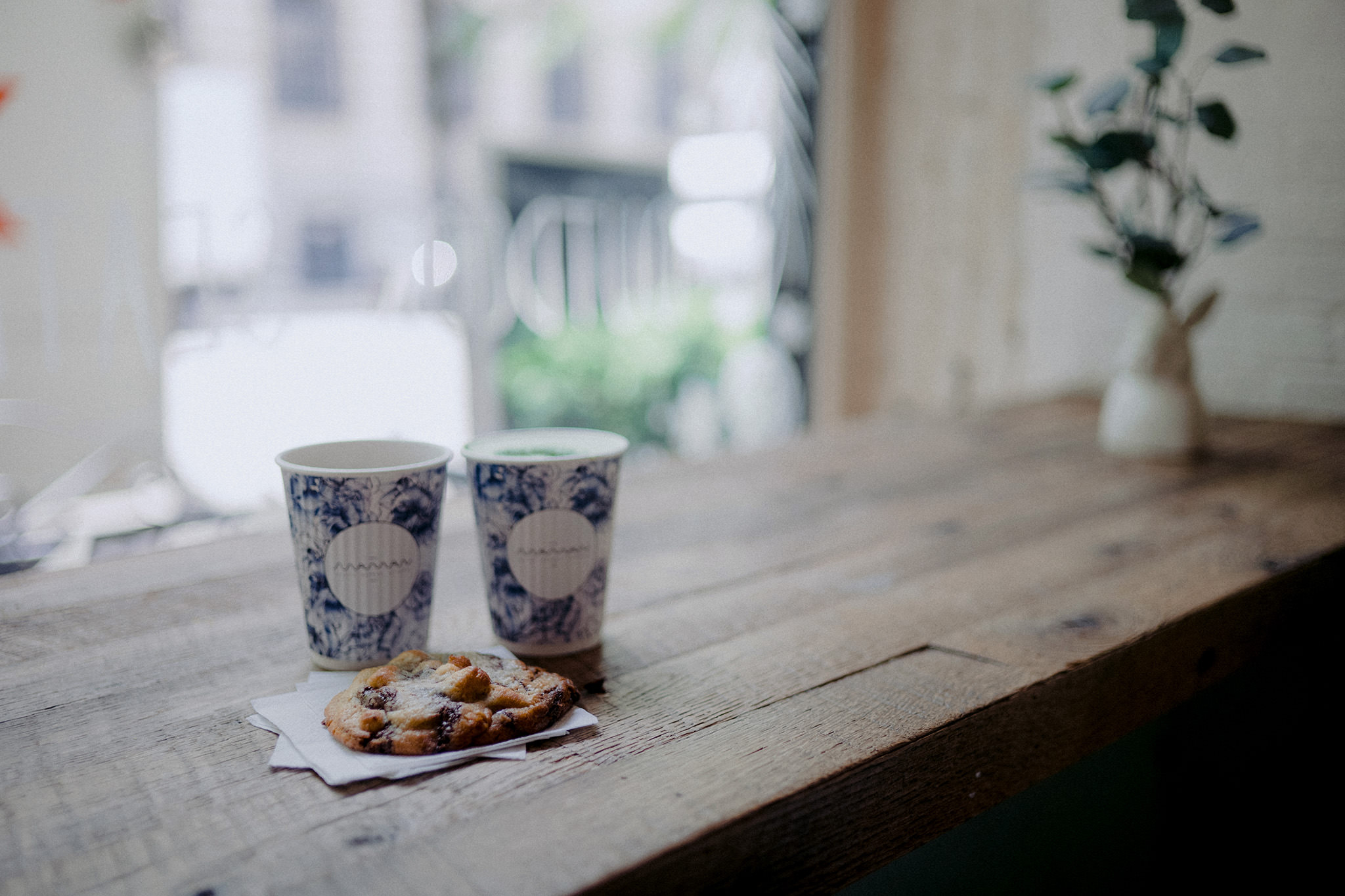 A chocolate chip cookie and two coffees at a cafe