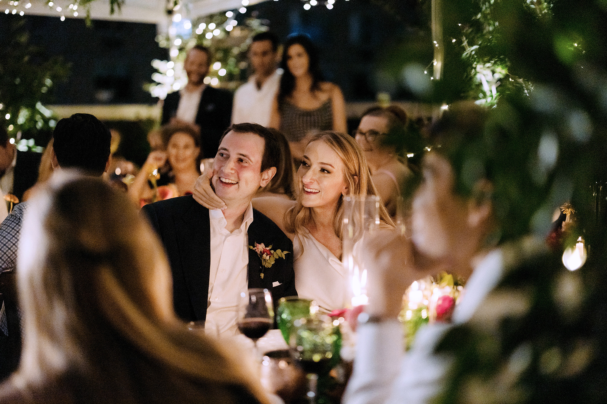Bride and groom look loving at their wedding guests over candle lit dinner