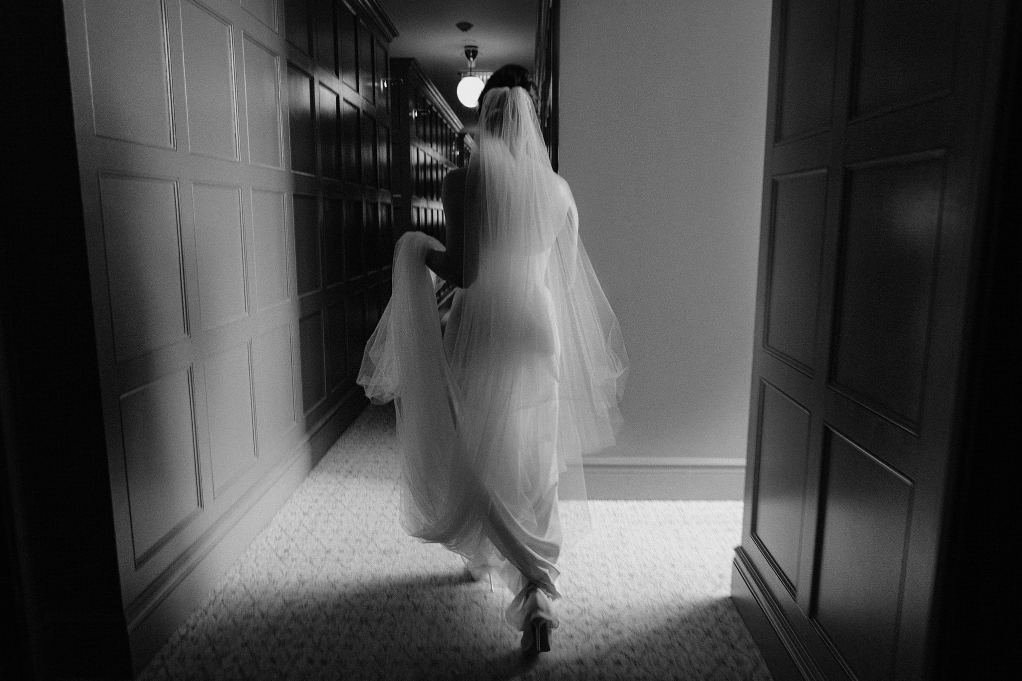 Bride walking down a hallway holding her gown and veil