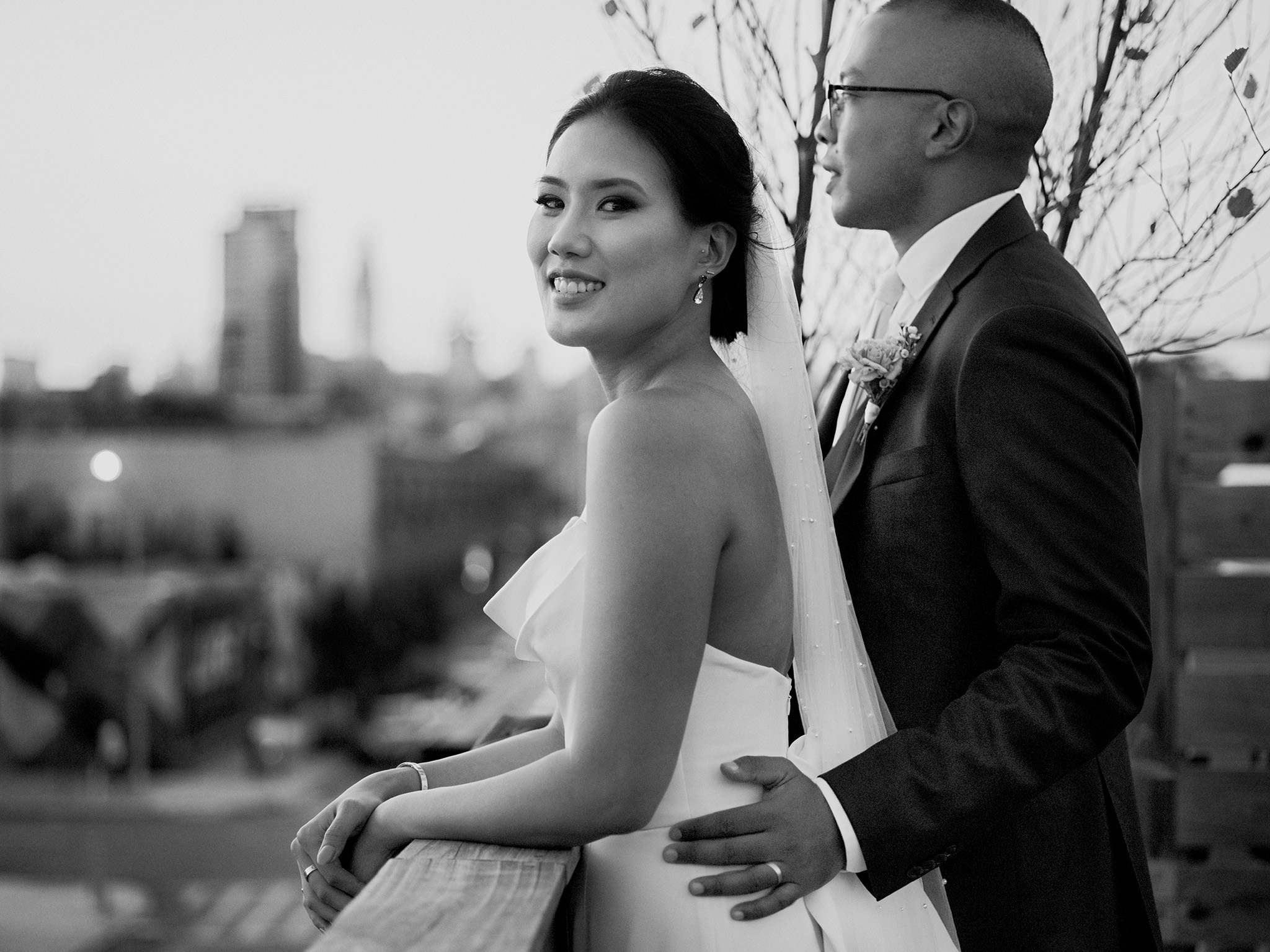 Groom with his hand on his brides waist looking out over Brooklyn, NYC