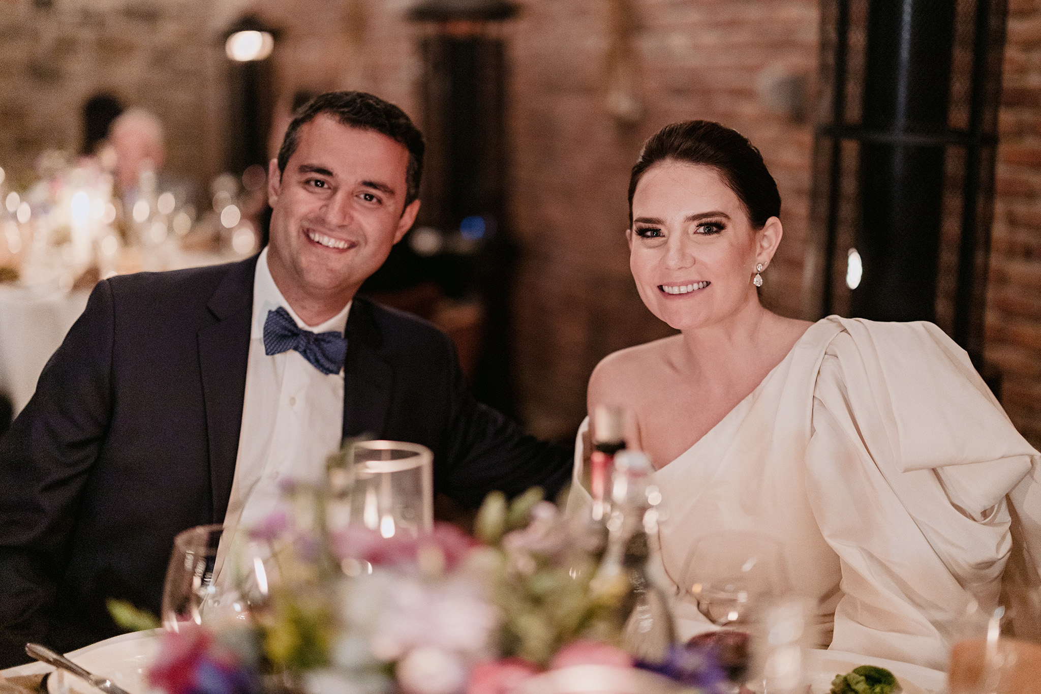 Bride and groom smiling at their wedding dinner reception lit by candles drinking wine.