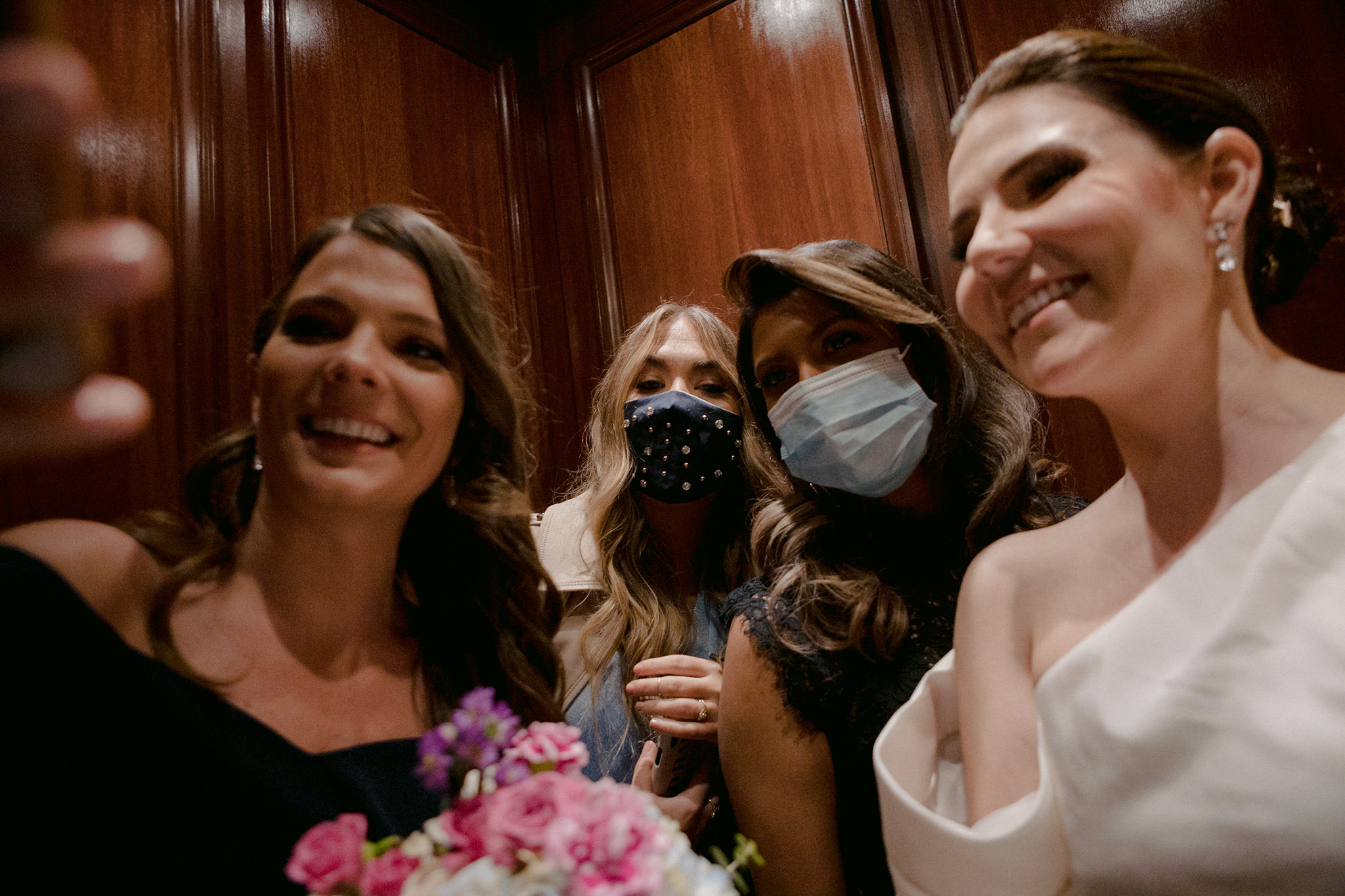 Bride and bridesmaids smiling for a selfie with masks on