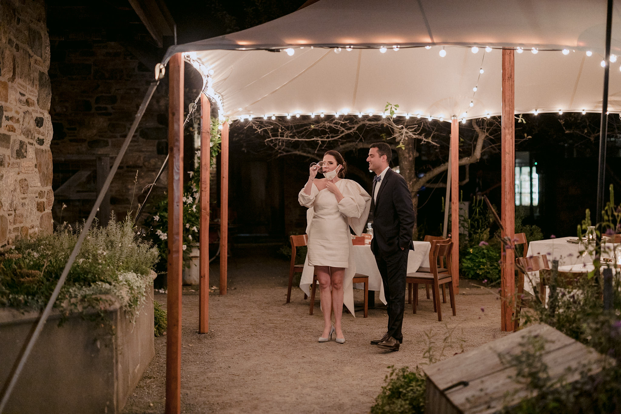 A bride sips her wine while lowering her COVID19 mask