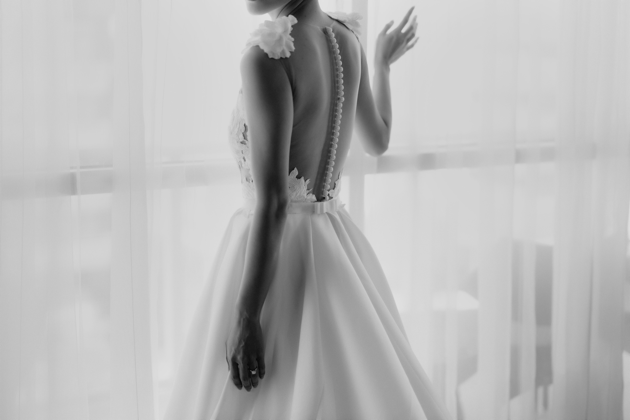 Brie stands in the window wearing a satin buttoned wedding dress