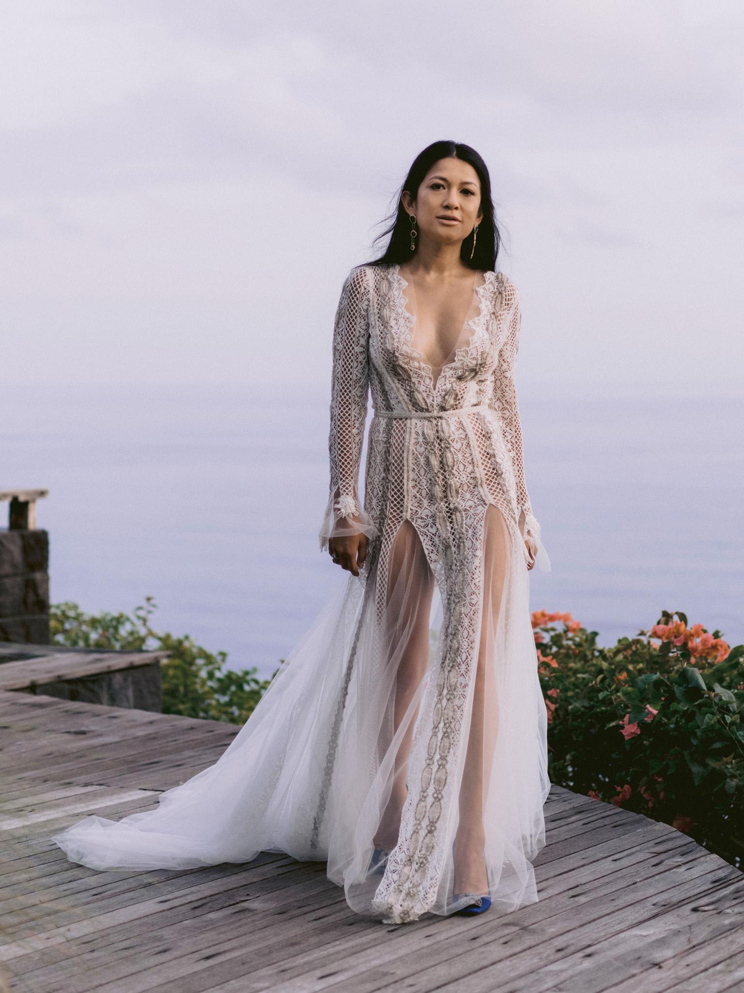 A woman stands in front of the ocean in her wedding dress