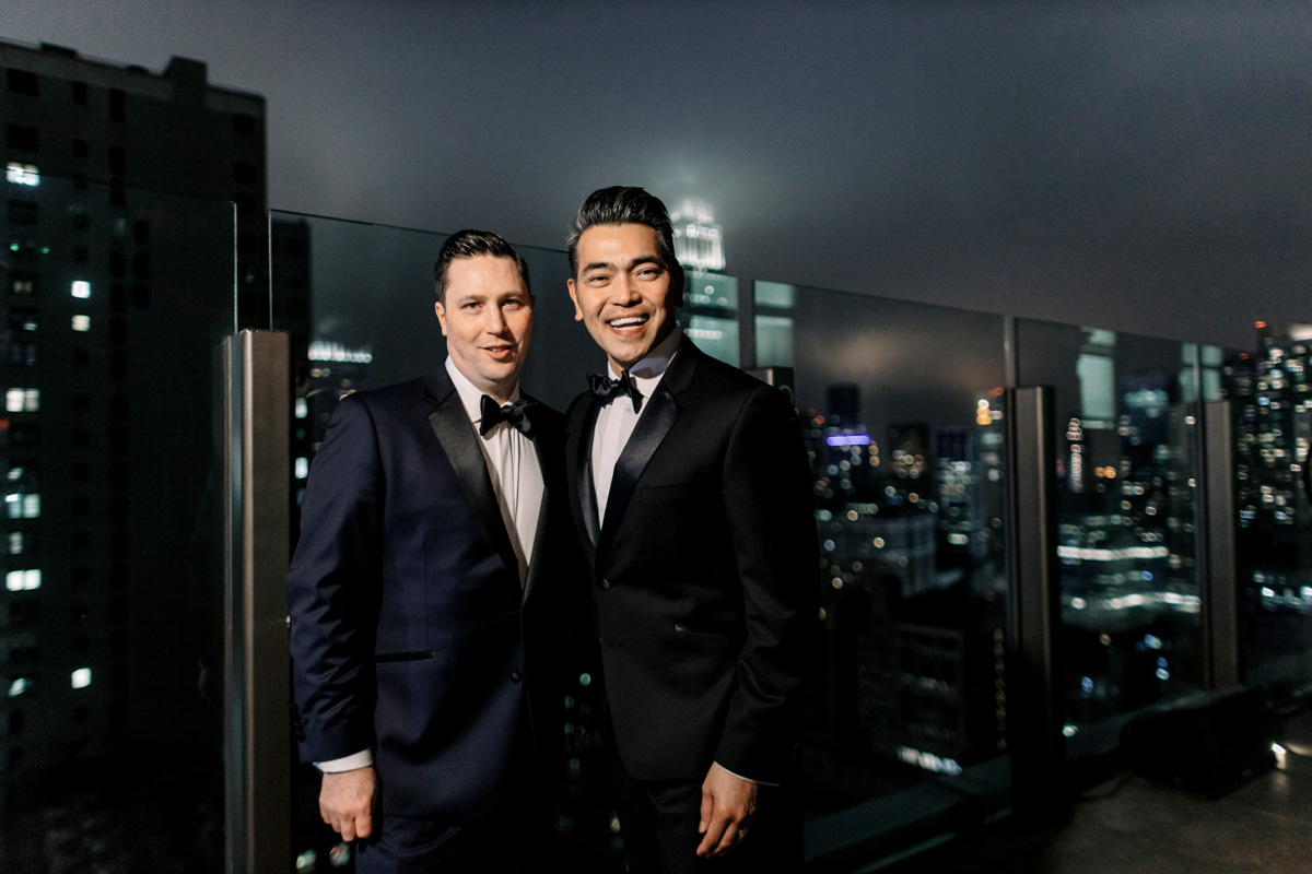 A gay couple stands on a rooftop with the Empire State Building in the background