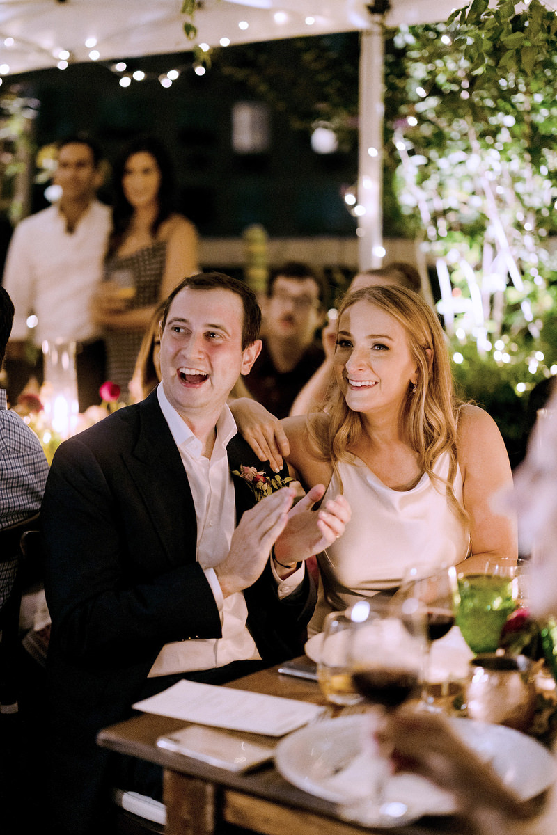 A bride and groom clap during speeches at their anniversary reception