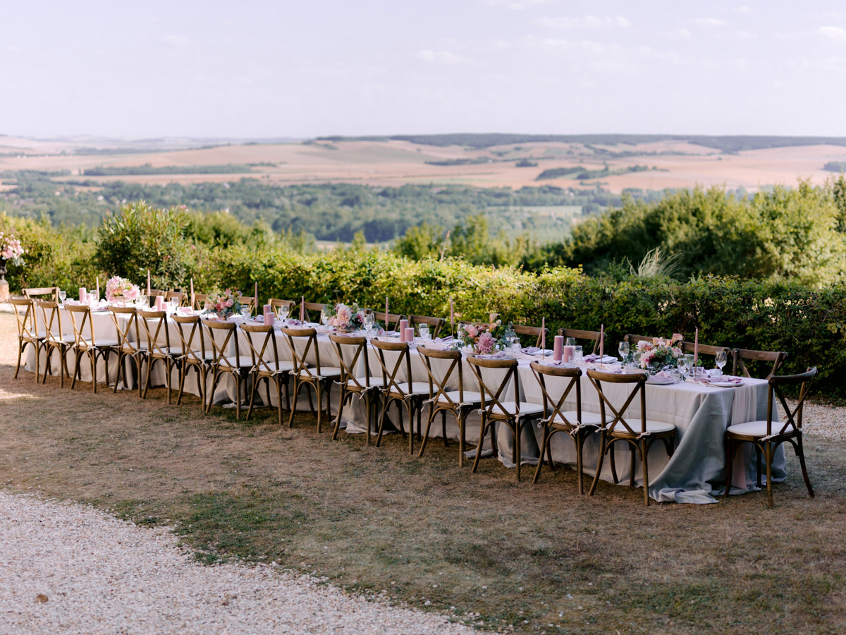 A long table sits on a grassy knoll at the destination wedding in France