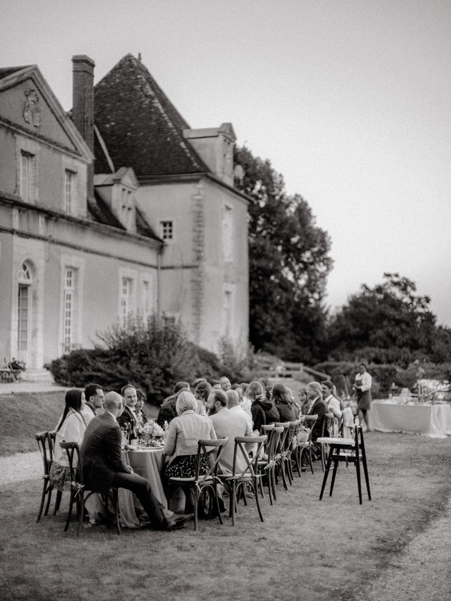 Guests of a destination wedding in France sit at a long table in a garden
