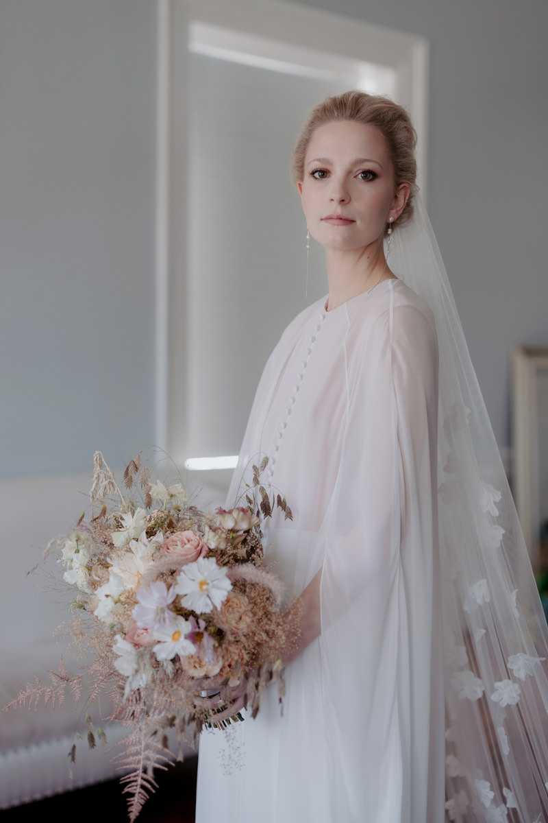 Blonde bride looks into the camera holding her bouqet