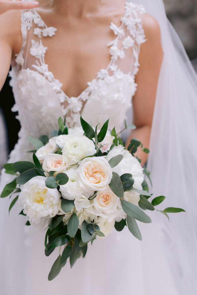 A bride holds her white floral bouquet while the wedding photographer takes her picture