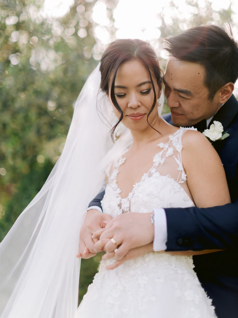 A groom embraces his bride and her veils blows in the wind.
