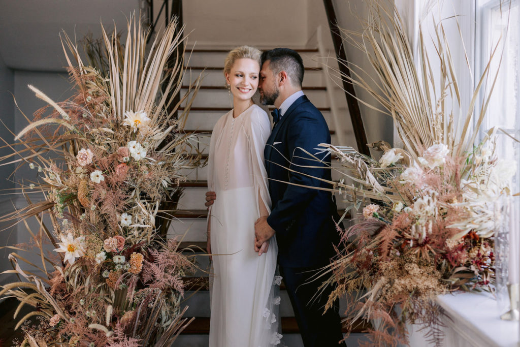 A bride and groom hold hands in front of a wooden staircase