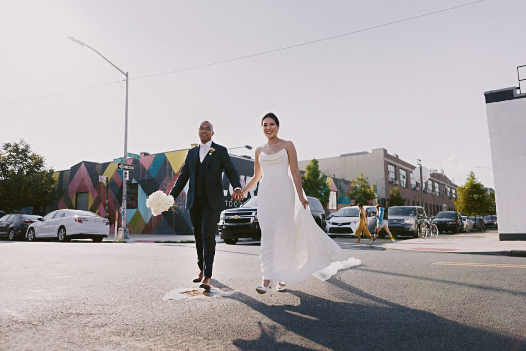 A bride and groom hold hands walking down Dobbin St in Brooklyn
