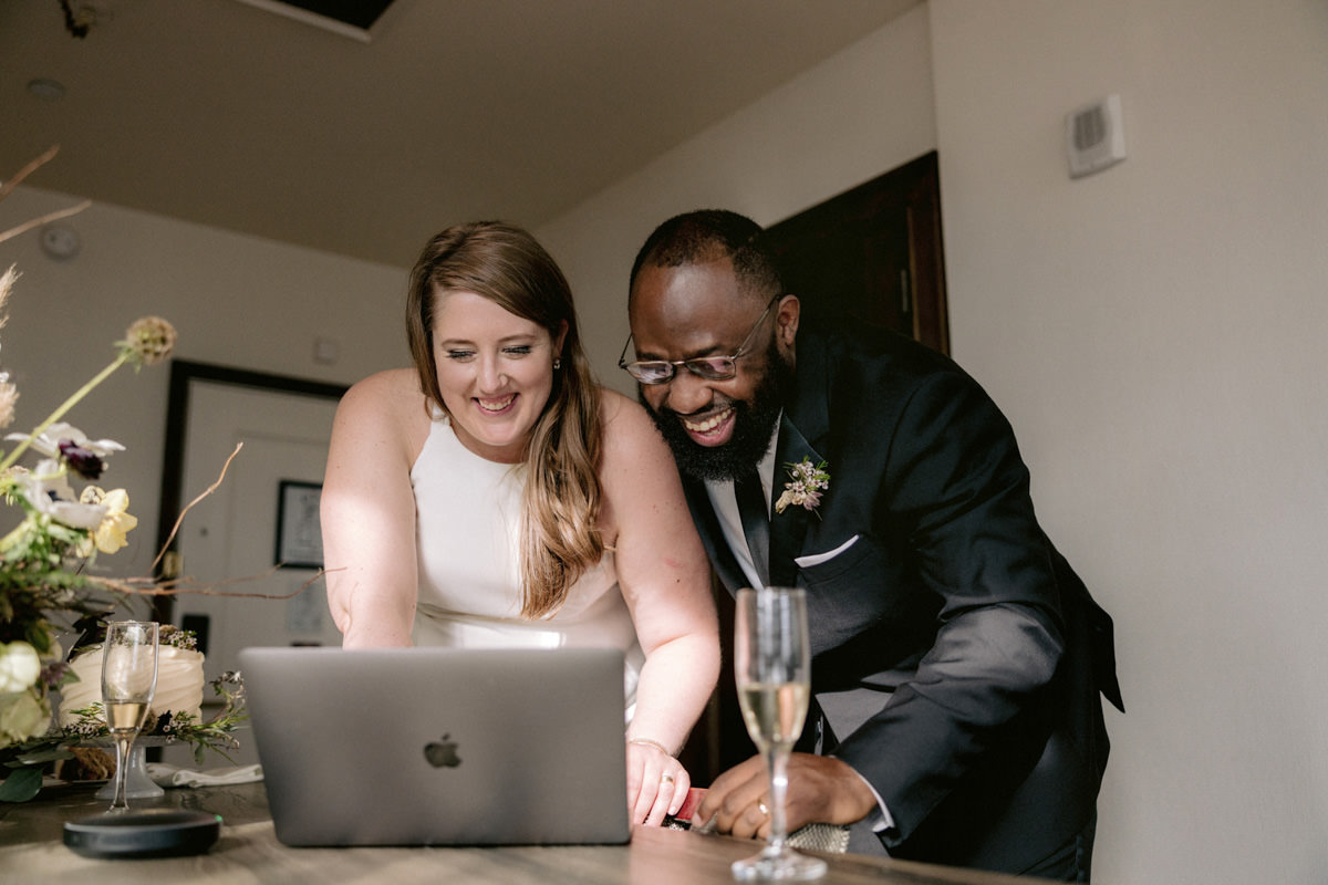 A biracial bride and groom smiling at their guests virtually