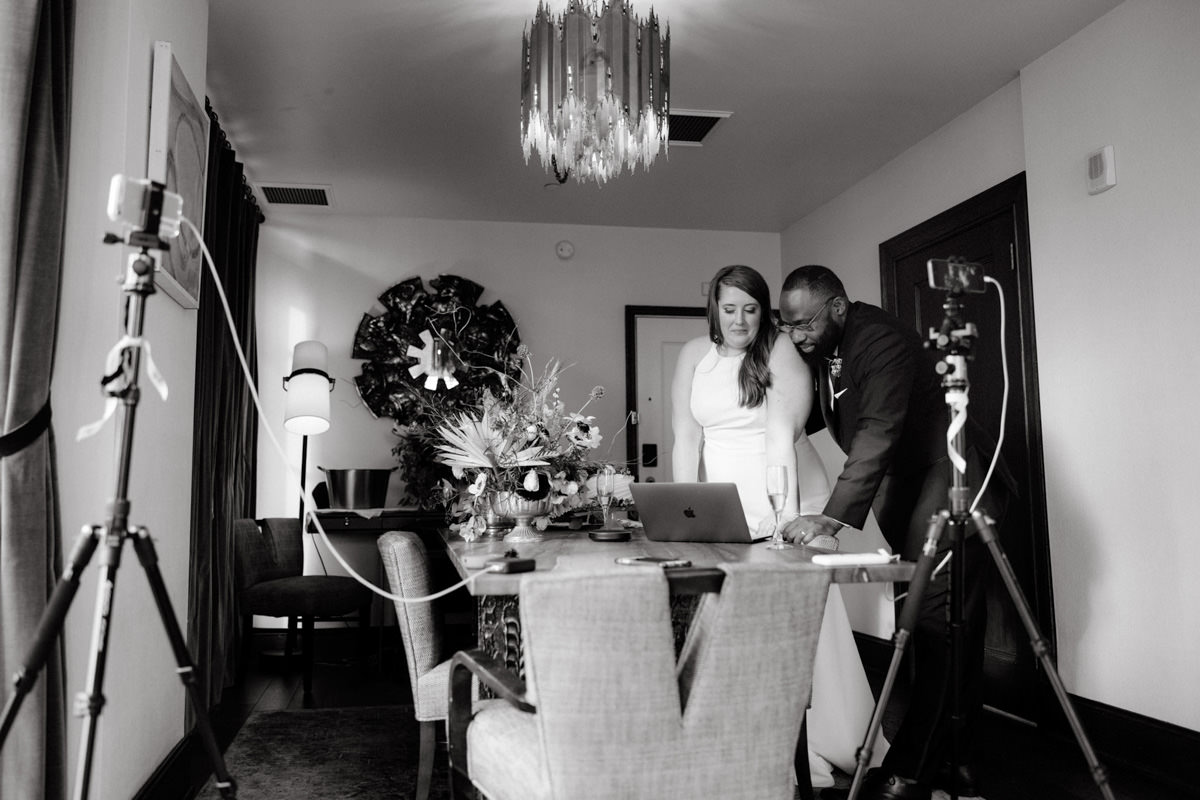 A bride and groom looking at a laptop with cameras surrounding them