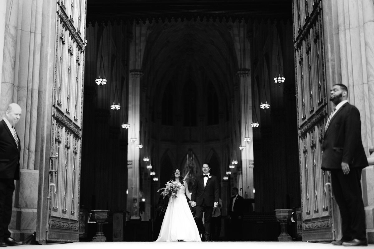 A bride and groom walk out the massive doors at St Patricks Cathedral in New York City