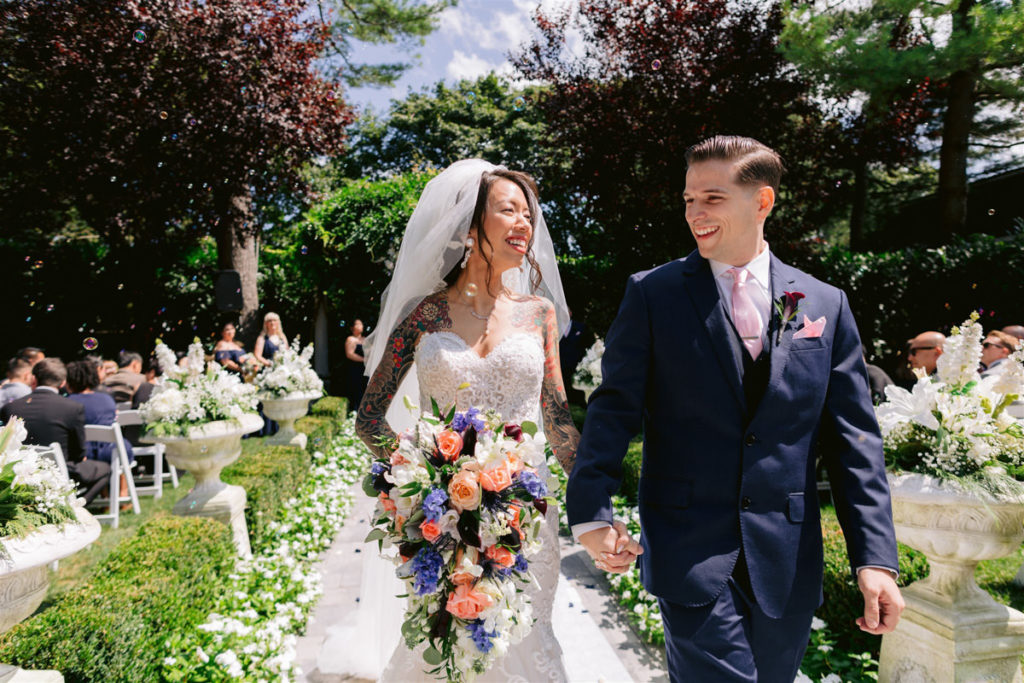 Bride and groom walk hand in hand down the aisle.