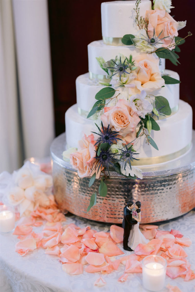 A white wedding cake with pink rose petals