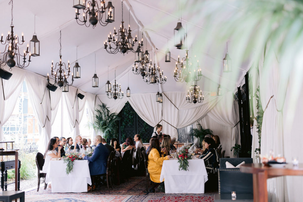 A white tent with vintage chandeliers and plants.