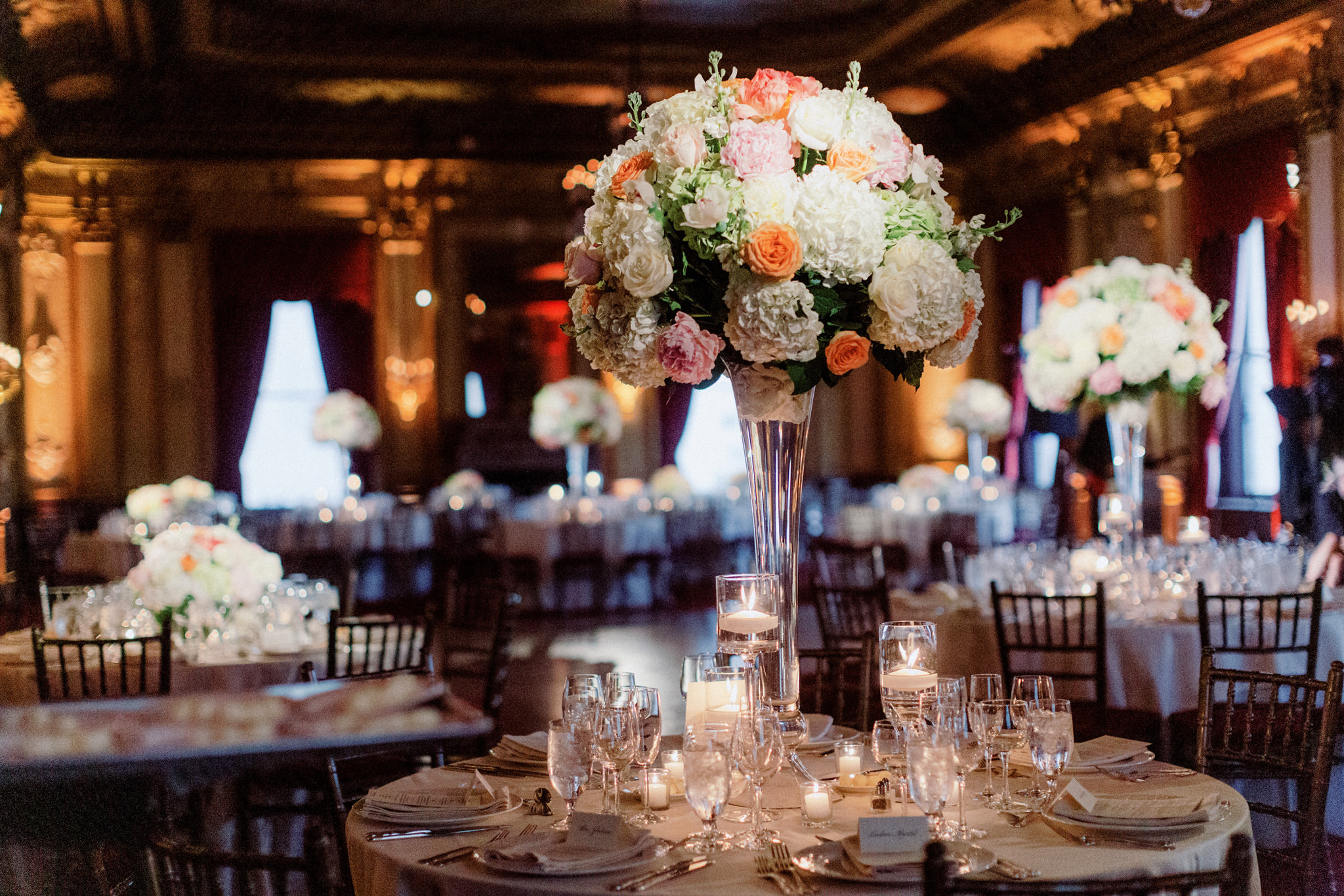 Tall centrepieces on a circular table with white, orange, and pink flowers