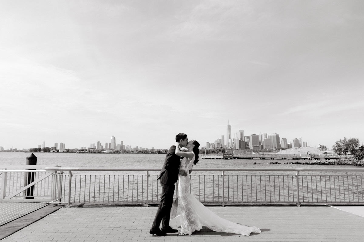 A bride and groom kiss with with the New York City skyline in the background