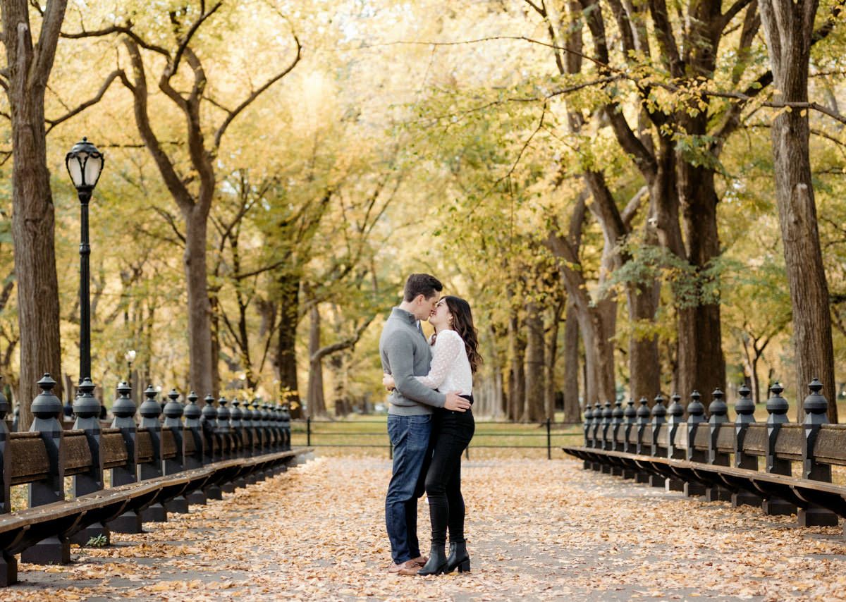 A man and woman kissing. Trees and fallen leaves on the background