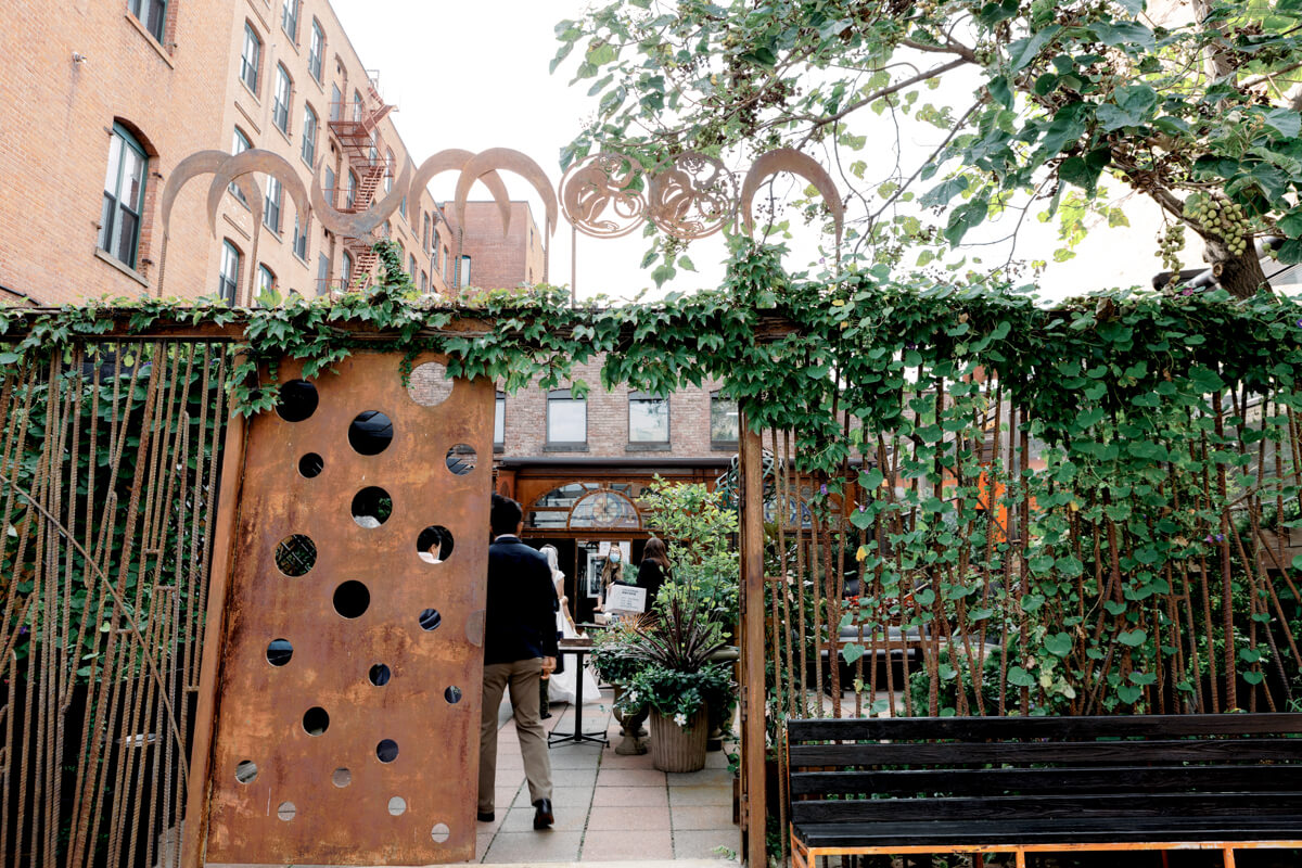Large, wooden door with holes in it and green vines on both sides of the door, and a black bench; people and plants inside