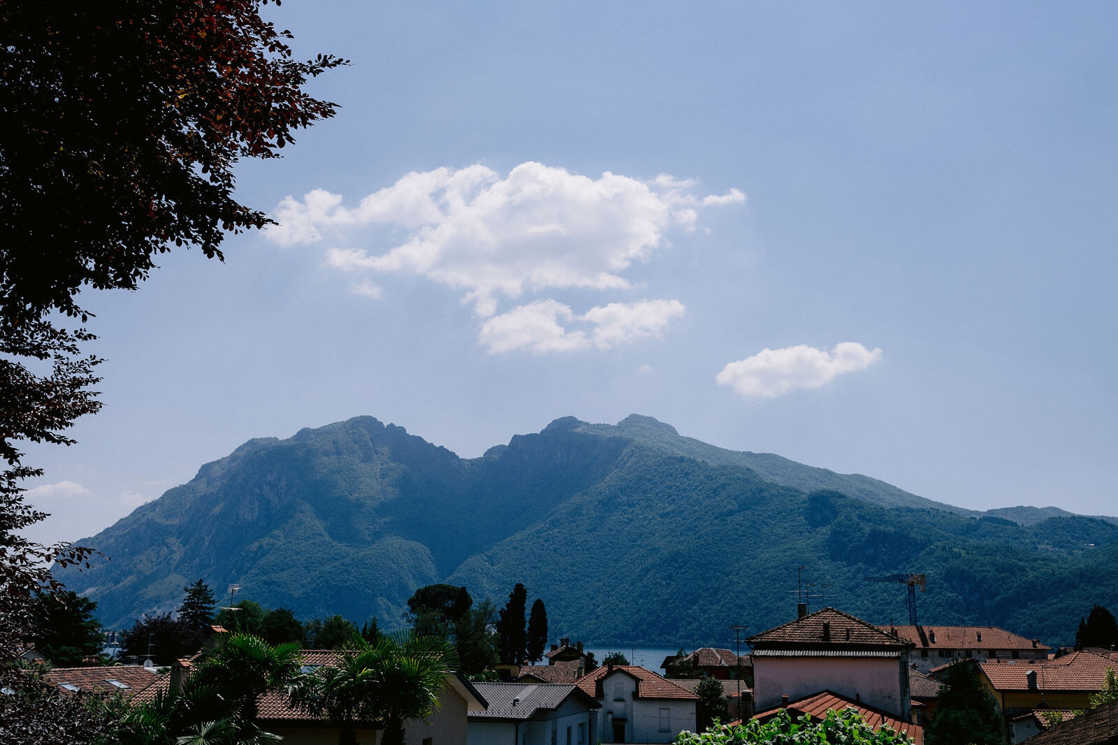 Many houses, some trees, with a large mountain and sky with white clouds on the background